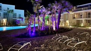 Un complexe hôtelier ouvert la nuit, doté d’une piscine, de palmiers et de chaises longues.
