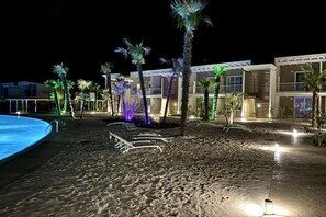 A beachfront hotel with a pool, palm trees, and outdoor seating areas. - Wave Island 4- Carraro Immobiliare Jesolo (Lido di Jesolo)