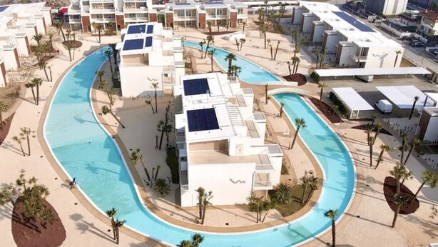 Un complex turístic amb una gran piscina, diversos edificis i palmeres.