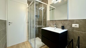 Une salle de bain moderne avec une douche à l’italienne en verre, un lavabo blanc et un meuble-lavabo foncé.