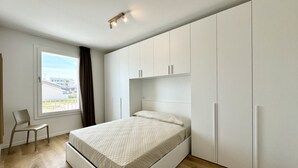 Een slaapkamer met een bed, een stoel, een raam en witte kasten.