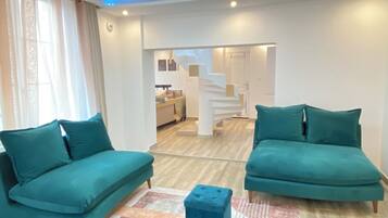 Ein modernes Wohnzimmer mit türkisfarbenen Sofas, einem zentralen Couchtisch und einer Treppe, die in eine obere Ebene führt.