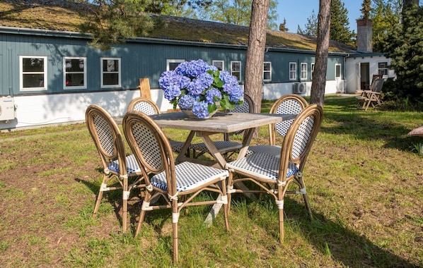 Une table en bois avec quatre chaises, un vase de fleurs bleues et une maison en arrière-plan.