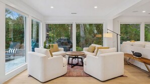 Una sala de estar moderna con sofás blancos, una mesa de centro redonda y grandes ventanas con vistas al exterior.