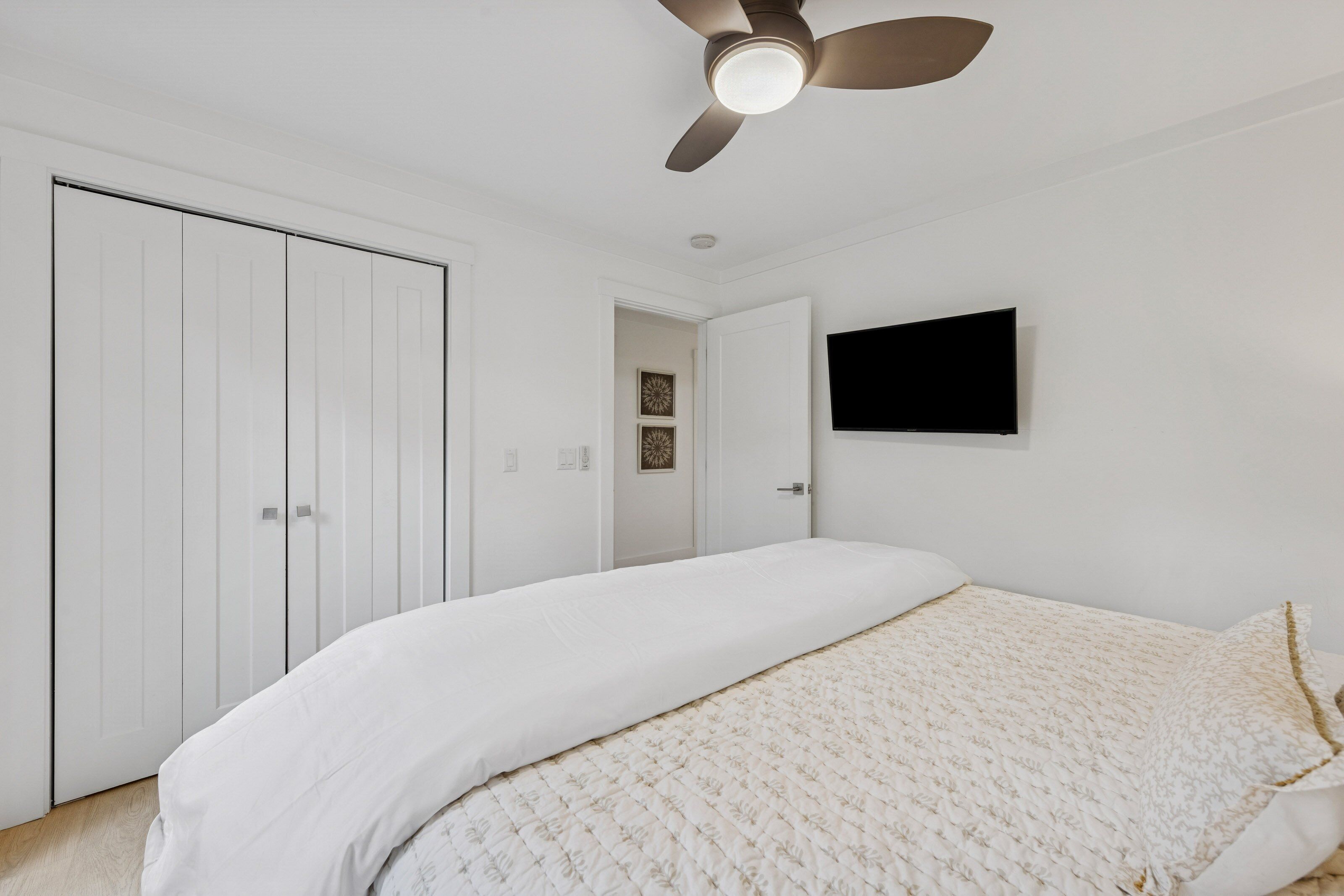 A bedroom with a bed, a ceiling fan, a TV mounted on the wall, and a wardrobe.