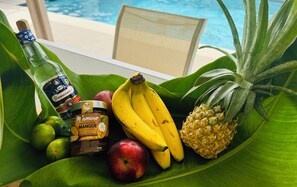 A table with a bottle of alcohol, a jar of mango preserve, bananas, an apple, and a pineapple on a green leaf. - Nakolodge 2 chambres - piscine / jardin privatifs  (Sainte-Anne)