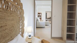 A bedroom with a woven headboard, a bedside lamp, a large bed, and a wooden wardrobe. - Nakolodge 2 chambres - piscine / jardin privatifs  (Sainte-Anne)