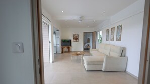 A spacious living room with a beige sofa, a small wooden table, and a TV. - Nakolodge 2 chambres - piscine / jardin privatifs  (Sainte-Anne)