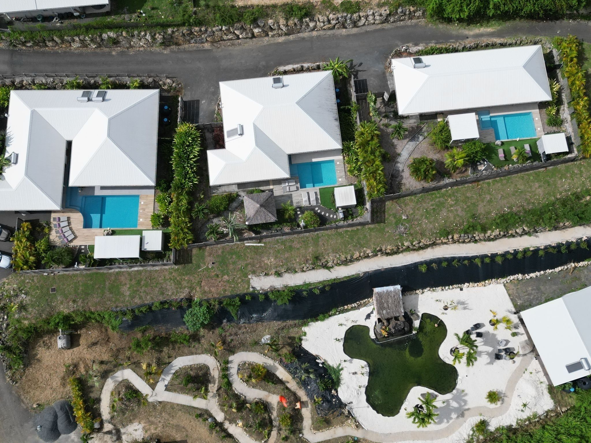 A residential area with multiple houses, each featuring a swimming pool and surrounded by greenery.