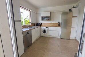A compact kitchen with a washing machine, a built-in oven, and a refrigerator. - Nakolodge 2 chambres - piscine / jardin privatifs  (Sainte-Anne)