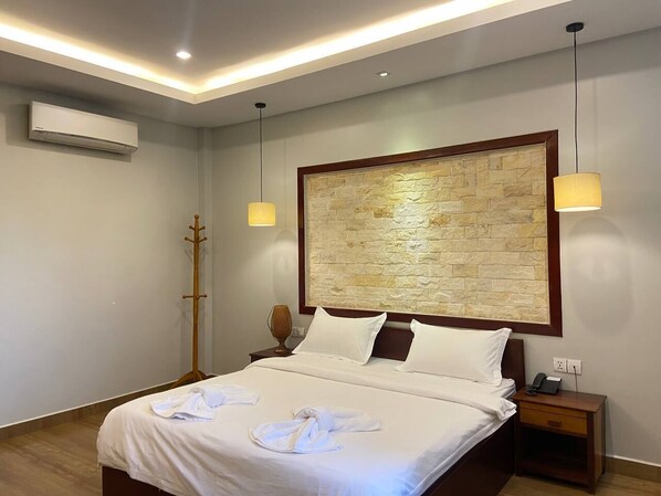 Una habitación de hotel con una cama grande, una mesita de noche de madera, un aire acondicionado montado en la pared y una pared de acento con textura de piedra.