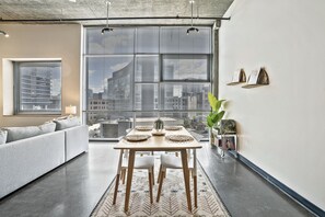 Un salon moderne comprenant une table à manger, un canapé et de grandes fenêtres donnant sur la ville.