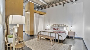 A bedroom with a bed, bedside tables, a lamp, a chair, and a rug. - *NEW* Trendy & Central Gulch Condo! (Nashville)