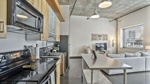 A modern kitchen with a built-in microwave, stove, and sink. There is a dining area with a sofa and a table. The room has a large window with a city view. - *NEW* Trendy & Central Gulch Condo! (Nashville)