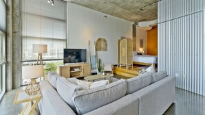 A modern living room with a grey sofa, a TV, a lamp, and a dining area. - Stylish 2 Bedroom in the Gulch (Nashville)