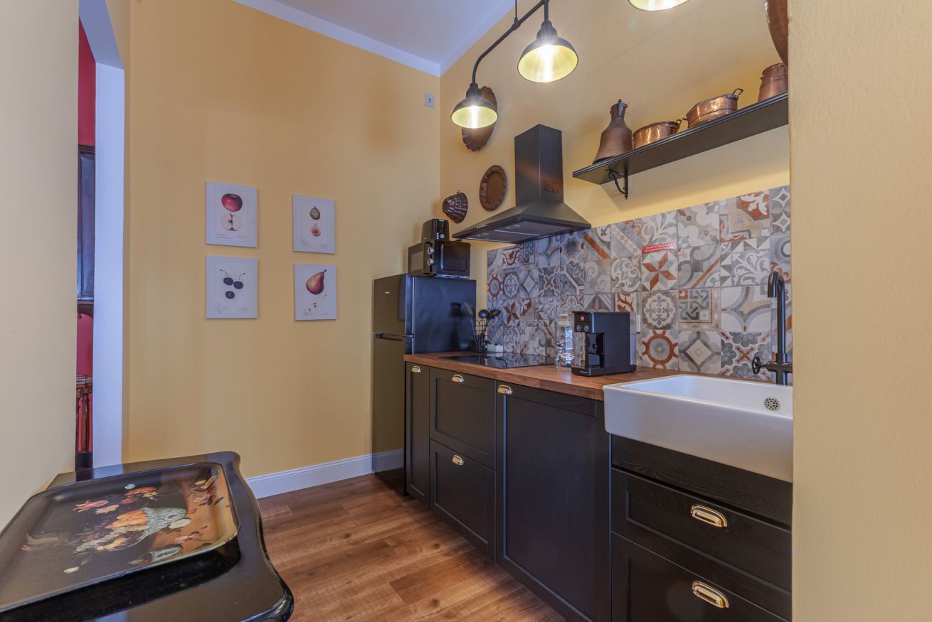 Een kleine keuken met donkere kastjes, een houten aanrecht, een spoelbak en een spatwand met decoratieve tegels.