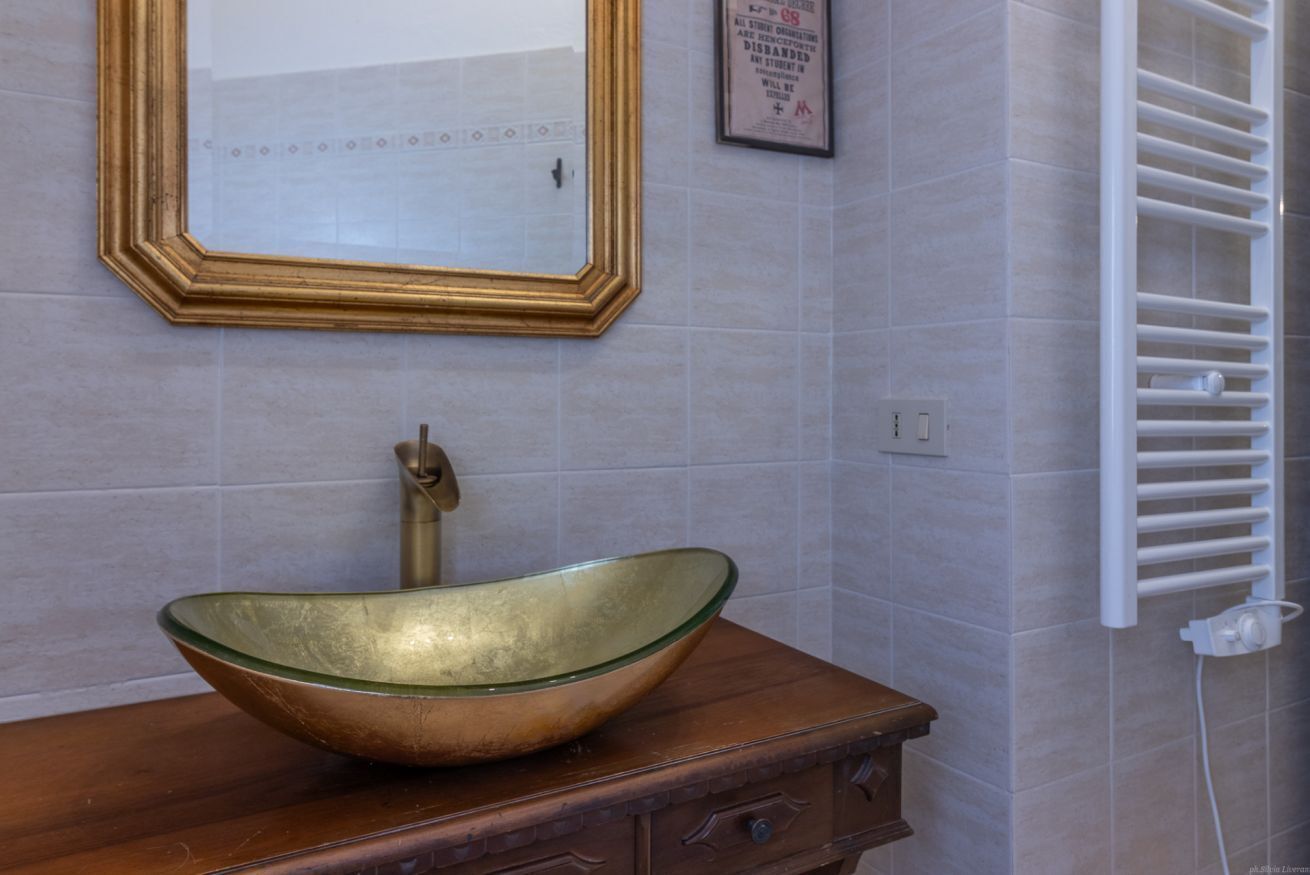 Een badkamer met een houten wastafelmeubel, een glazen wasbak, een spiegel met gouden lijst en een handdoekhouder.