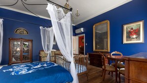 Een slaapkamer met een hemelbed, een houten bureau, een stoel en een grote spiegel.