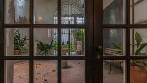 Uitzicht door een raam met een rasterpatroon, potplanten, een bank en een met bakstenen bestraat pad.