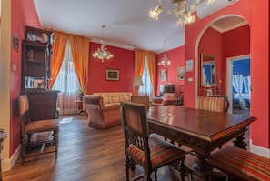 A dining area with a wooden table and chairs, a sofa, and a chandelier. - GuestHost - The House of Harry Potter and a Love Story (Ferrara)
