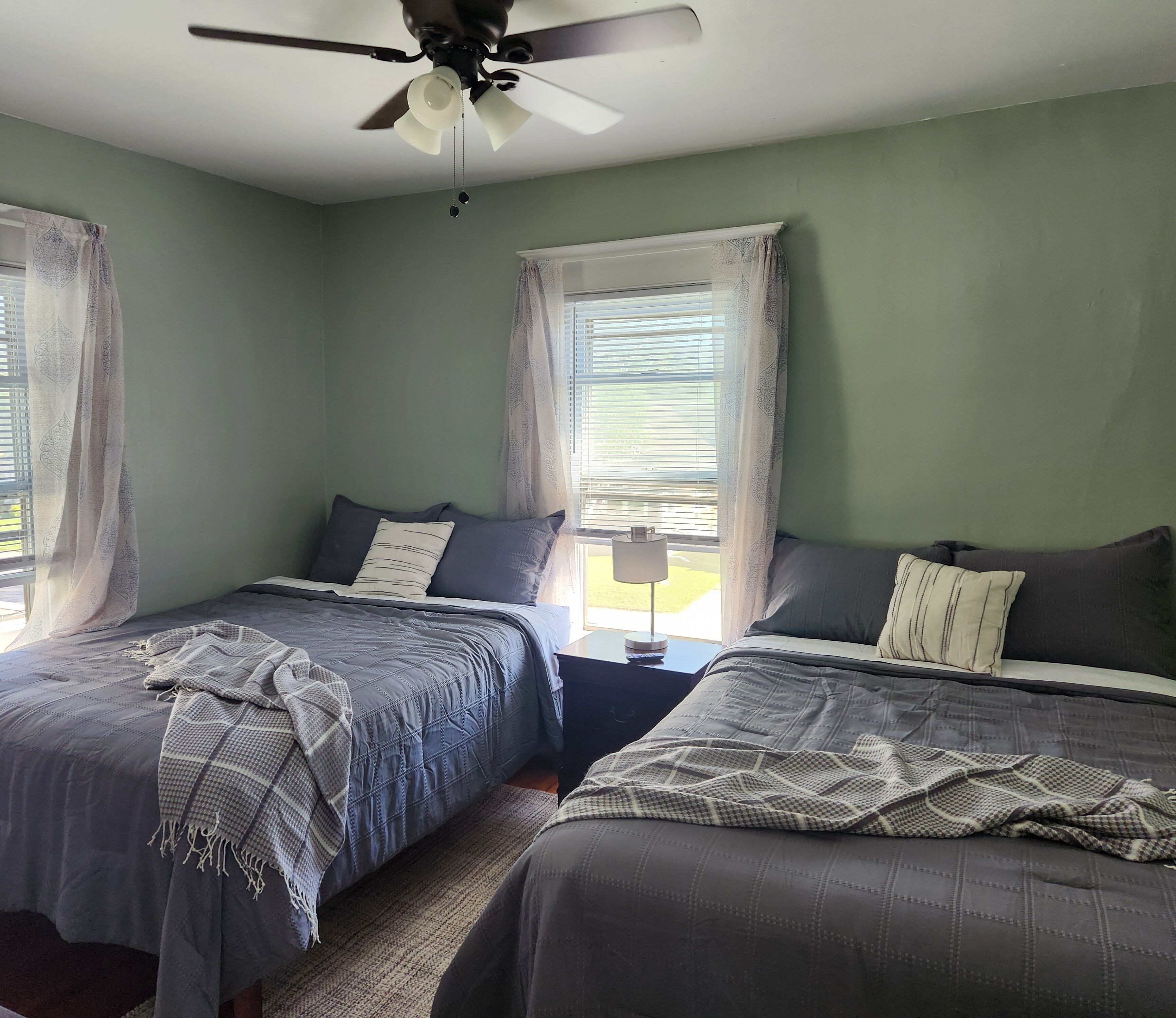 A bedroom with two beds, a ceiling fan, and a window with blinds.