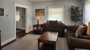 Ein Wohnzimmer mit einer Couch, einem Couchtisch, einer Lampe, einer Pflanze und einem Fenster mit Jalousien.