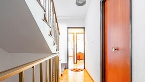 A hallway with a wooden door, a staircase with a handrail, and a tiled floor.