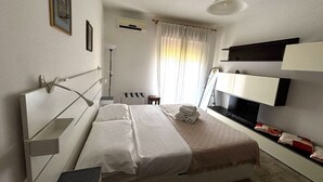 A hotel room with a bed, bedside tables, a TV, a lamp, and a window with curtains.