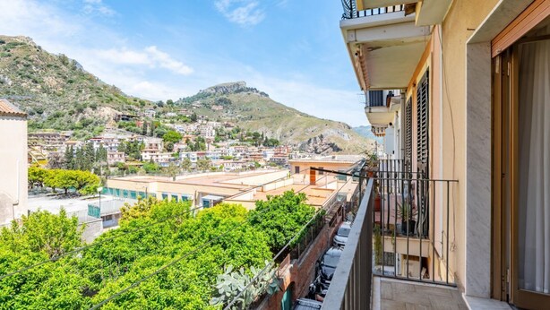 A balcony with a view of a hillside town, a clear sky, and a building with a balcony.