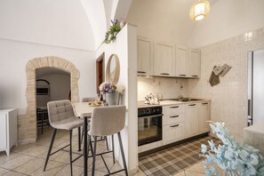 Une cuisine avec des meubles blancs, une arche en pierre et un coin repas avec deux chaises.