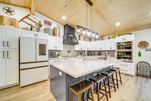 Une cuisine moderne avec des meubles blancs, un grand îlot central doté de tabourets, et divers appareils électroménagers, notamment un réfrigérateur, un four et une machine à café.