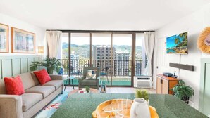 A modern living room with a sofa, a dining table with a tray, a chair, and a view of a cityscape through large windows.
