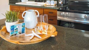 A kitchen counter with a tray holding a pitcher, glasses, a plant, and a welcome sign.