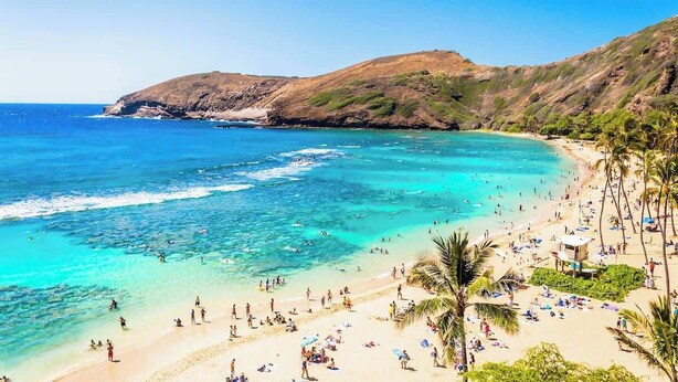A beach with clear turquoise waters, a sandy shore, and a mountainous backdrop.