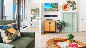 A living room with a sofa, a coffee table with fruit, a TV, and a wall-mounted guitar.