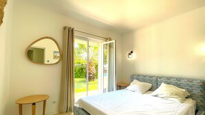 Una camera da letto con un letto, uno specchio rotondo, un tavolino e una porta scorrevole in vetro che dà su un giardino.
