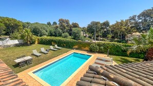 Una piscina rettangolare con bordo piastrellato, circondata da un prato e da una fila di lettini.