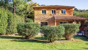 A two-story house with a tiled roof, surrounded by greenery and trees.