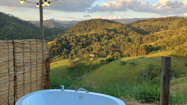 A hot tub on a wooden deck with a view of a mountainous landscape. - EMBAHÚ SUÍTES  (Santo Antonio do Pinhal)