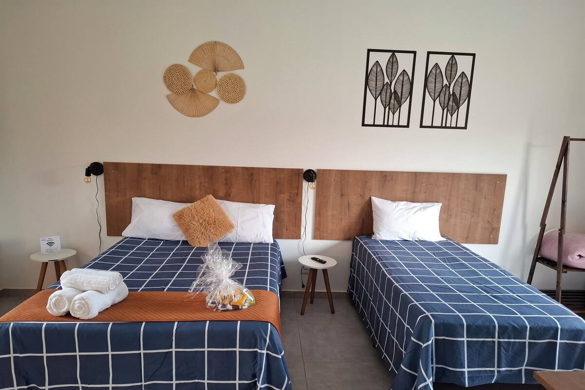 A hotel room with two beds, each with a blue checkered bedspread, a wooden headboard, and a wall-mounted light fixture.