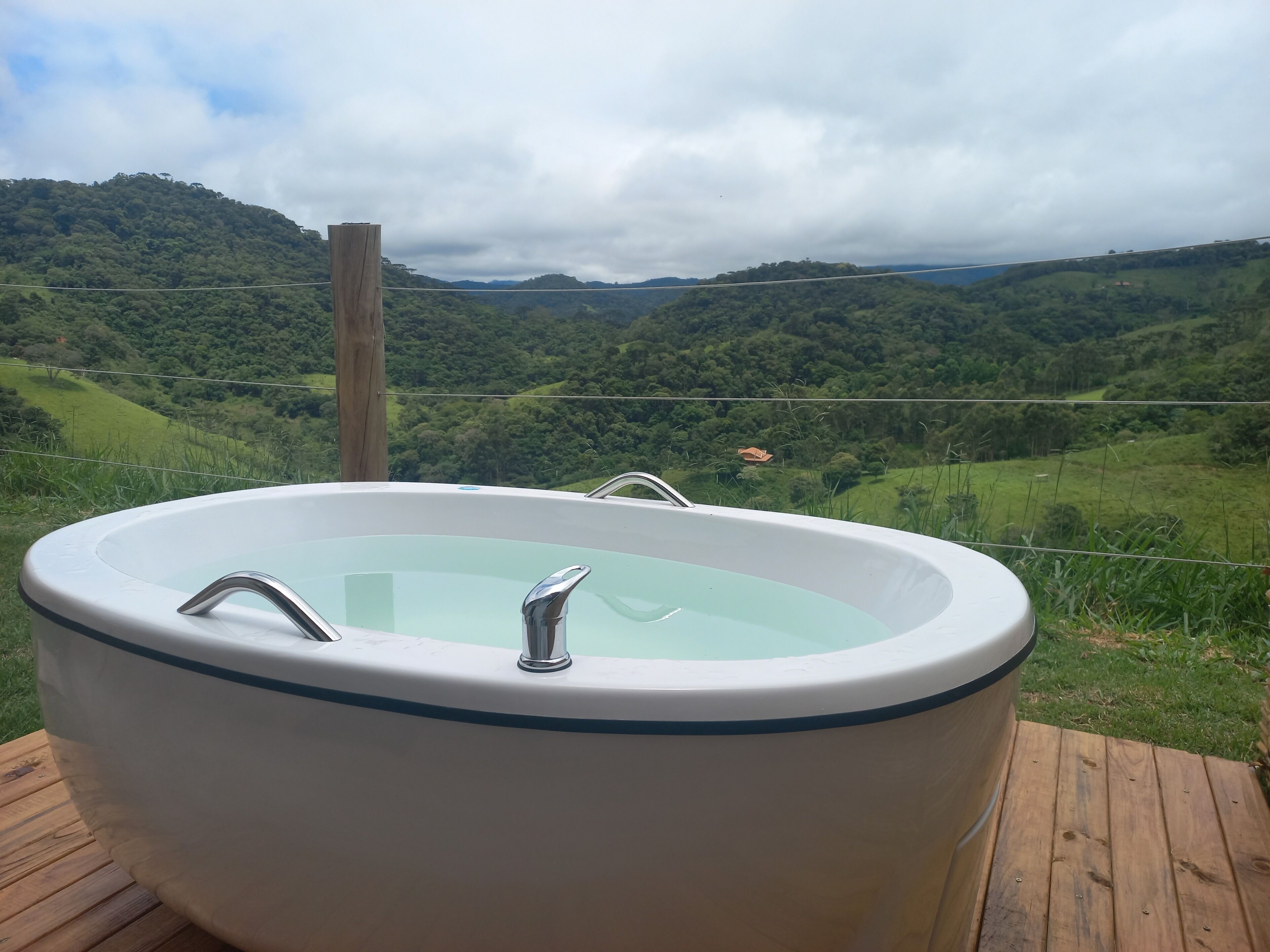 Een hottub op een houten terras met uitzicht op een weelderige vallei en heuvels.
