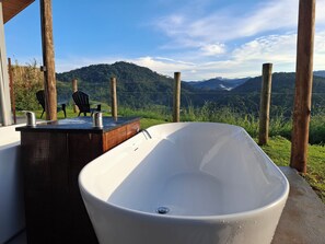 A bathroom with a freestanding bathtub, wooden counter, and a view of a mountainous landscape. - EMBAHÚ SUÍTES  (Santo Antonio do Pinhal)