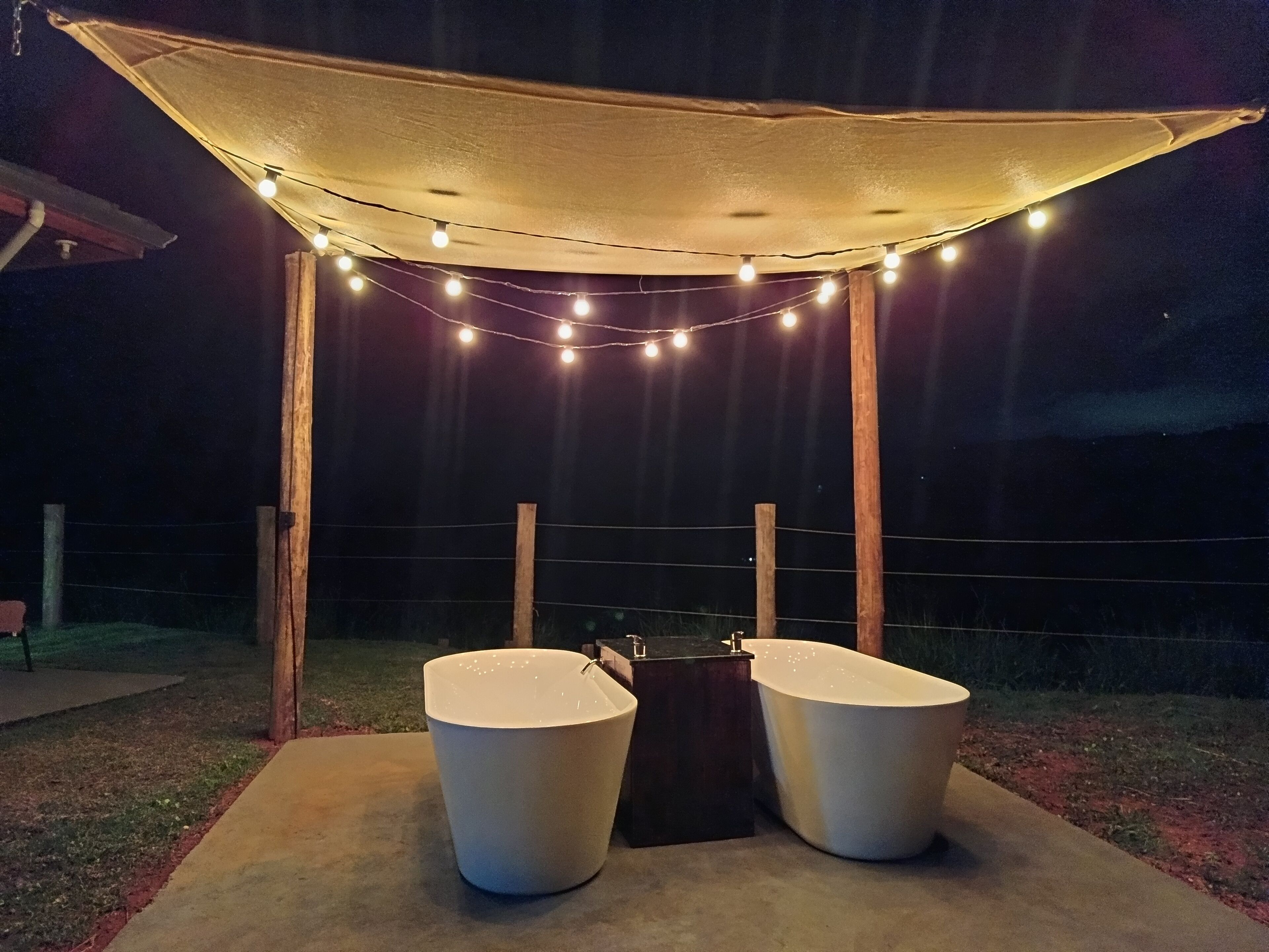 An outdoor seating area with two white planters, a canopy, and string lights.