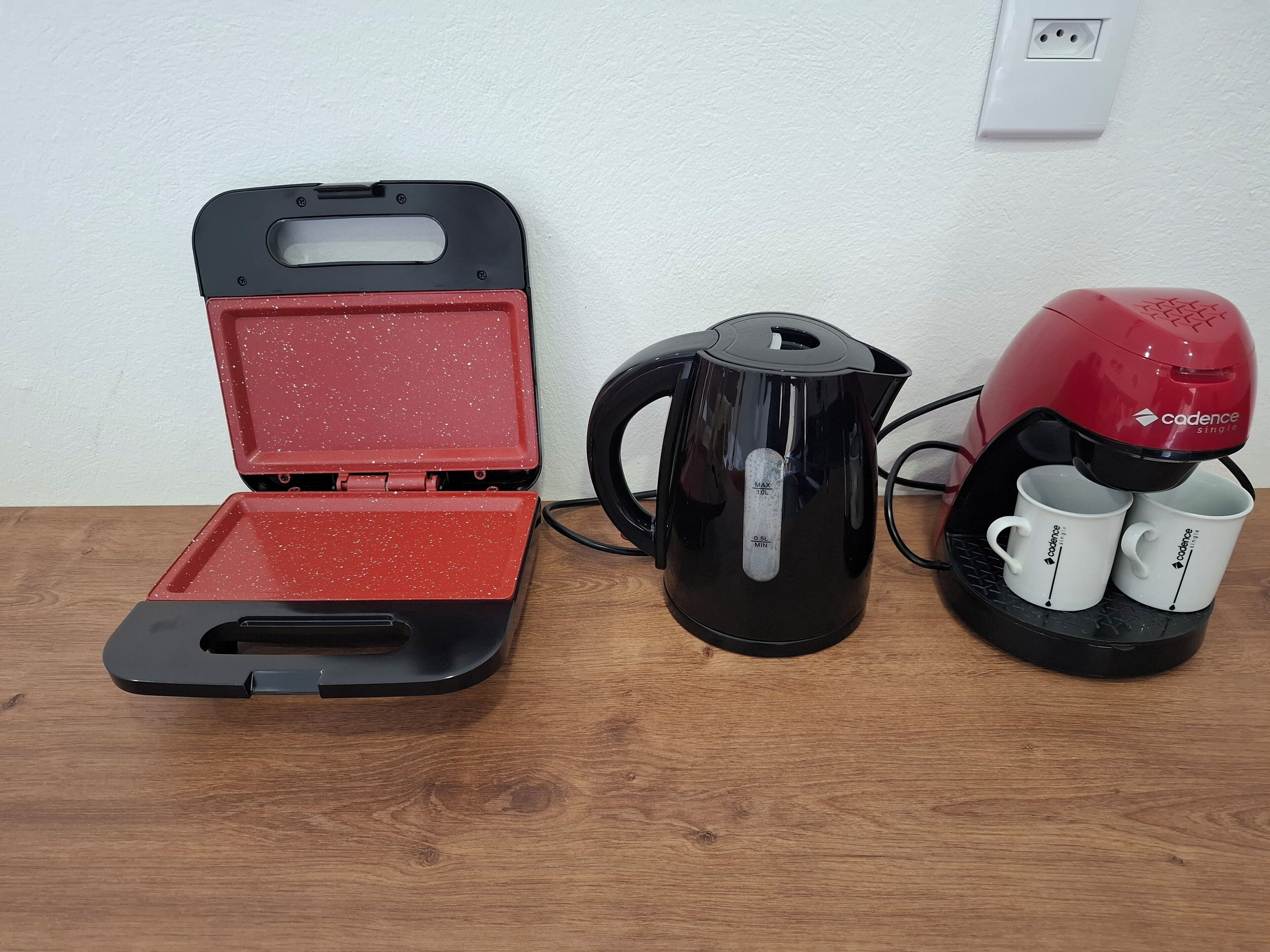 Una cafetera, un termo y un hervidor eléctrico portátil sobre una mesa de madera.