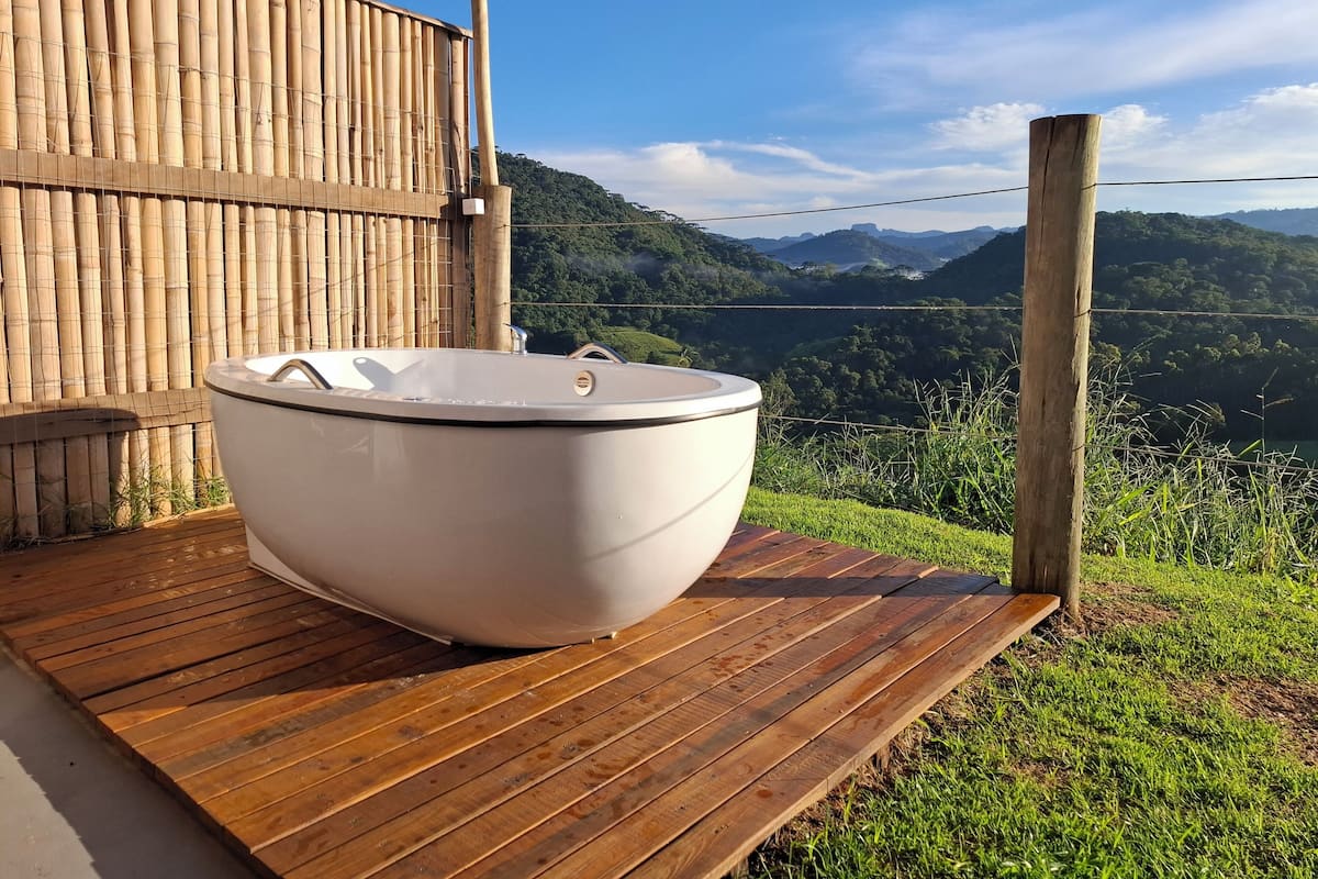 A hot tub on a wooden deck with a bamboo fence and a scenic view of hills and mountains.