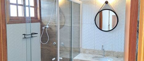 Un baño con ducha de vidrio, un zócalo de madera, un espejo redondo con luz y un lavabo con encimera.
