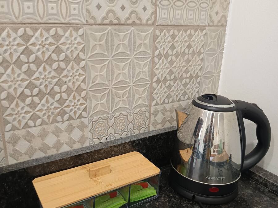 A kitchen with patterned tiles, a black countertop, a wooden cutting board, and a stainless steel kettle.