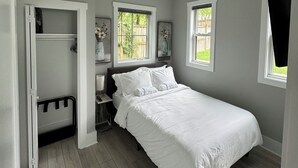 A bedroom with a bed, a walk-in closet, and a window with a view of greenery.