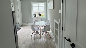 A modern kitchen with a dining area, white cabinetry, and a window with blinds.