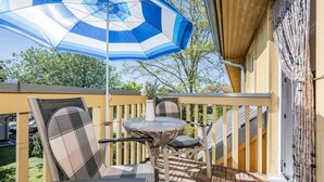 A wooden deck with a table and chairs, a blue and white striped umbrella, and a bamboo decoration.